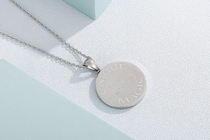 Close-up of a silver stainless steel round pendant engraved with Unique and Magic