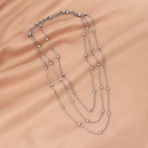 Macro view of triple-layered silver bead chain necklace on champagne silk background