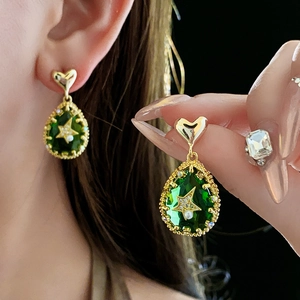 Macro detail of vintage green teardrop earrings with gold stars and pearl accents
