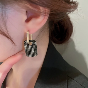 Détail de boucles d'oreilles dorées géométriques avec breloques rectangulaires noires