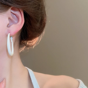 Close-up of elegant white glossy hoop earrings on female model with warm lighting