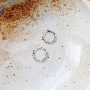 Elegant 925 sterling silver twisted hoop earrings resting in a rustic ceramic bowl
