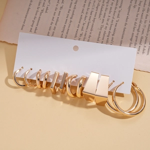Close-up of 5 pairs of minimalist golden C-shaped and geometric metal earrings set on a book