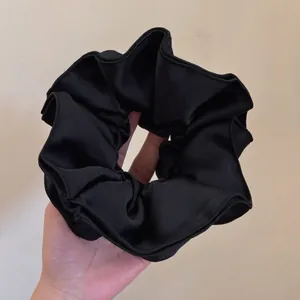 Detailed texture of black satin oversized scrunchie with elegant silk luster and pleats
