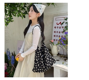 Detailed view of black canvas tote bag with white bow patterns in a sunny garden setting