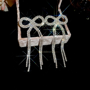 Detailed view of silver bow tassel earrings with sparkling rhinestones on velvet box