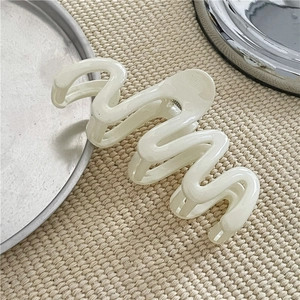 Close-up of white wavy hair claw clip with smooth glossy finish on woven background