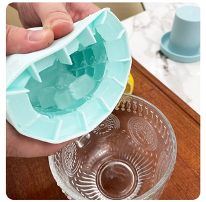 Hand squeezing light blue silicone ice bucket to release small cubes into a glass