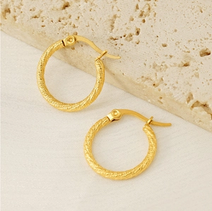 Detailed view of gold twisted hoop earrings on a minimalist stone background