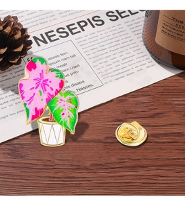 Detail of creative potted plant brooch with pink and green enamel leaves on a wooden table
