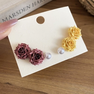 Detailed shot of resin rose earrings with pearls in red and yellow on display card