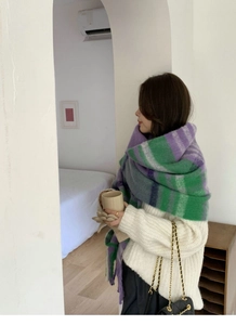 Detail view of large green and purple checkered scarf wrap worn over a white knit sweater