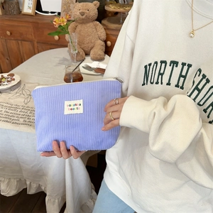 Macro shot of purple corduroy makeup bag with woven label in a cozy cafe setting
