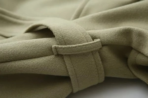 Detailed close-up of bean green wool coat stitching and texture on the belt loop