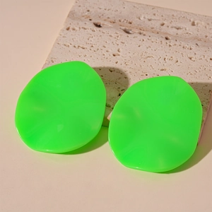 Close-up of bright neon green oval resin stud earrings on a textured stone base