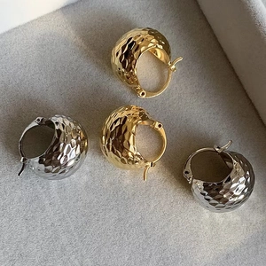 Vue détaillée des boucles d'oreilles martelées dorées et argentées sur plateau velours