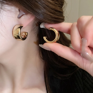 Détail de la boucle d'oreille créole en métal doré en forme de C avec fini poli miroir
