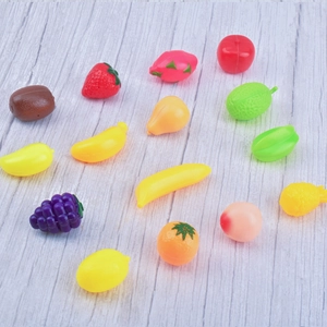 Miniature plastic fruit models for dollhouse props scattered on light wood background