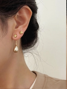 Detailed close-up of textured gold studs and smooth teardrop pendant earring on model