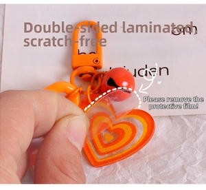 Removing protective film from an orange heart-shaped acrylic keychain with small red bell