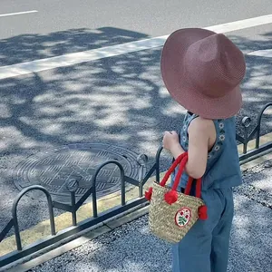 Dettaglio di un bambino che indossa un cappello di paglia rosa e un abito estivo blu ricamato