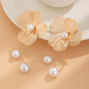 Detailed close-up of golden ginkgo leaf earrings with pearls on a ceramic plate