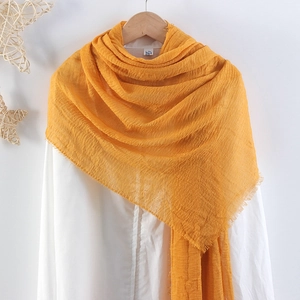 Detail of yellow crinkle cotton scarf with frayed edges hanging on a wooden hanger