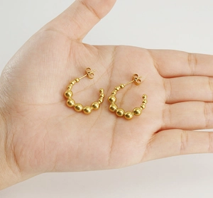 Close-up of 18K gold-plated C-shaped bead earrings held in palm to show relative size