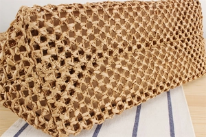 Close-up of natural straw hollow mesh weave and brown lining of a woven tote bag