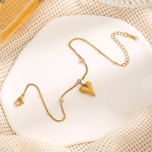Detailed close-up of golden heart pendant anklet with cubic zirconia on white ceramic tray