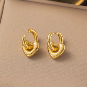 Pair of polished gold stainless steel hoop earrings with 3D heart pendants on a textured surface