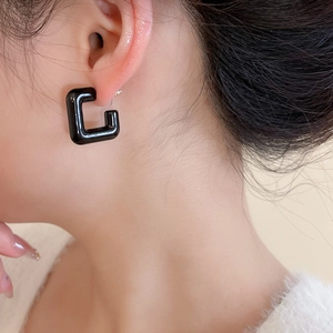Close-up of minimalist black acrylic C-shaped earrings worn on an ear for a stylish look