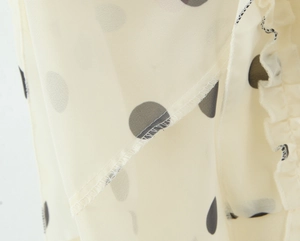 Detail shot of black polka dot pattern on beige chiffon fabric with ruffle edge