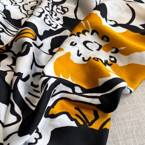 Close-up of soft silk scarf fabric with bold yellow and black floral print texture