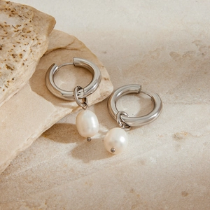 Silver stainless steel hoop earrings with white pearl pendants on textured stone