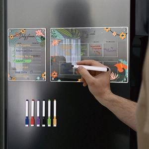 Close-up of magnetic acrylic weekly planner with floral patterns on a black fridge door