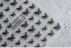Close-up of translucent dark butterfly nail art stickers on a soft plush background