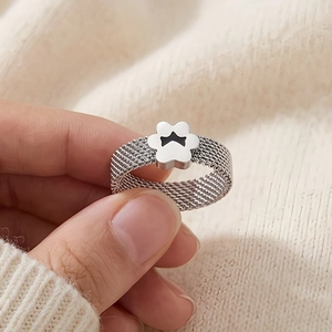 Close-up of silver mesh ring featuring white floral charm and black crown detail