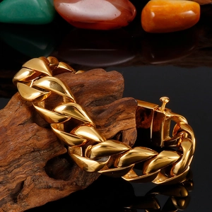 Close-up of golden Cuban link chain bracelet displayed on dark wood and colorful pebbles