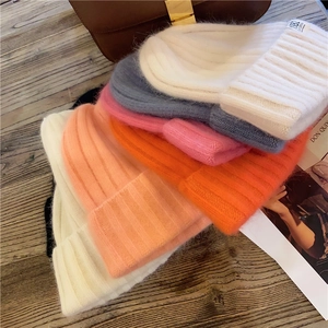 Stack of colorful knitted beanies in cream, orange, and blue with soft texture detail
