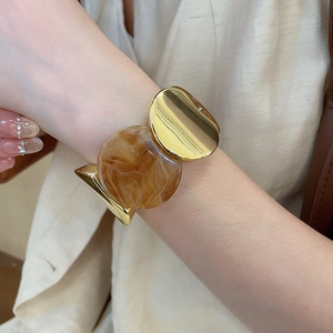 Détail d'un bracelet manchette doré avec une grande incrustation ronde en résine