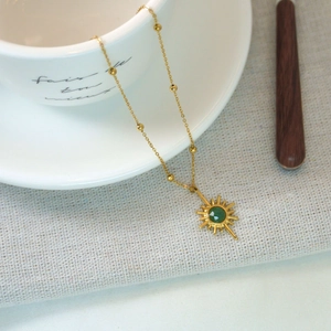 Detail of 14K gold plated necklace with green stone starburst pendant on table