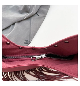 Detail of burgundy suede texture with silver zipper, metal studs and bohemian tassels