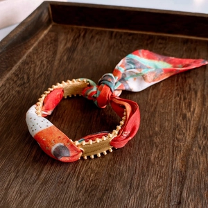 Detail of red floral fabric ribbon and matte gold buckle on a double-layer bracelet