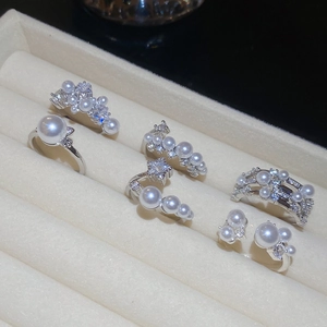 Detail view of silver zircon and pearl rings displayed in a beige velvet jewelry box