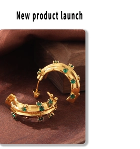Detail view of gold-plated C-shaped earrings with green glass stones and textured studs