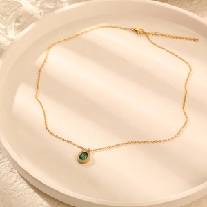 Vue détaillée du collier pendentif émeraude ovale avec halo de diamants sur plateau blanc
