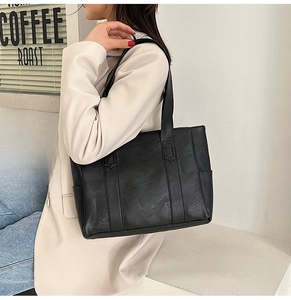 Detail of a black PU leather tote bag with wide straps worn by a model in a café