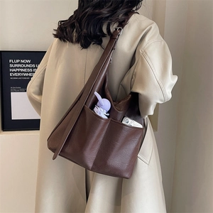 Detail showing the large brown leather tote bag with wide strap on model's shoulder