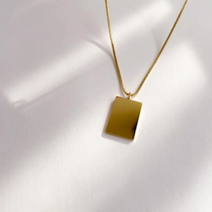 Close-up of minimalist gold box chain and rectangular pendant with a polished finish